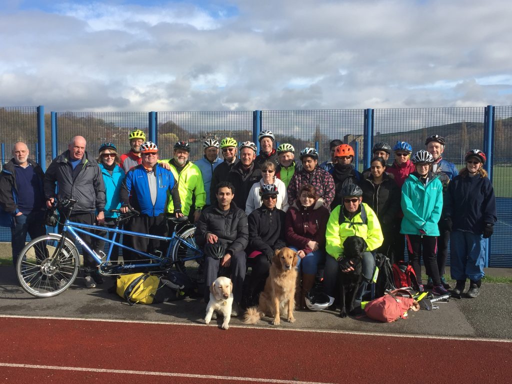 25 Trekkers and 3 Guide Dogs clustered around the bench at Leeds Road Track