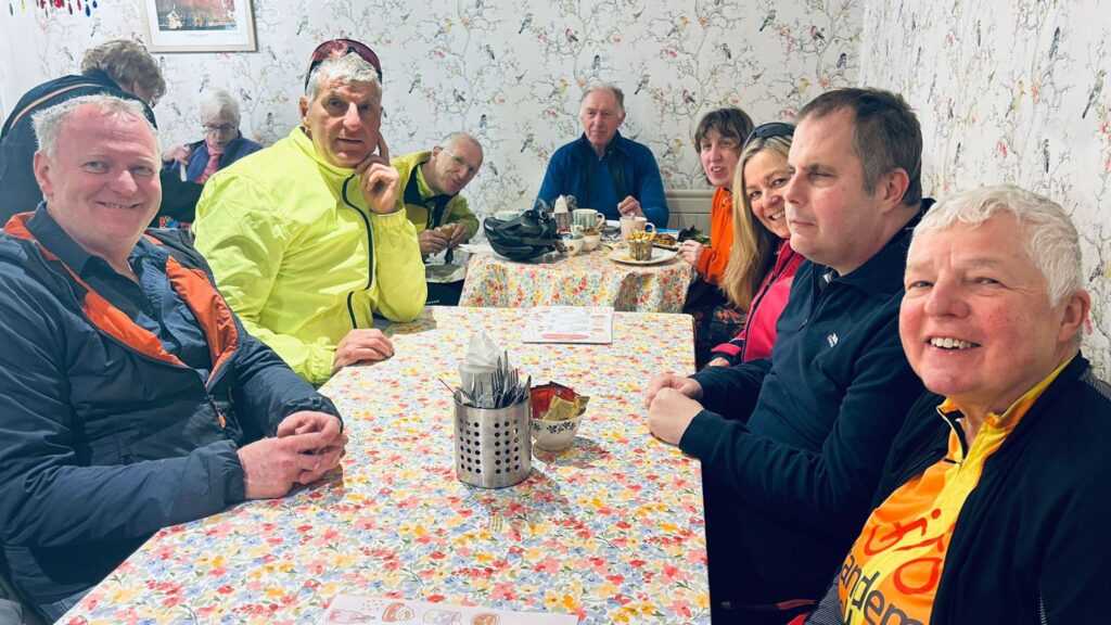 A group of Trekkers sat around a long table with pale floral wall paper on the cafe walls.