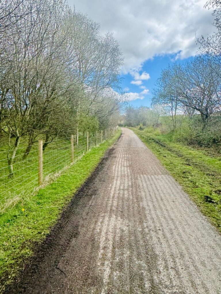 A long straight stretch of off road track with an even and unblemished surface stretches off into the distance, flanked my neat green grass and trees just coming into bed.