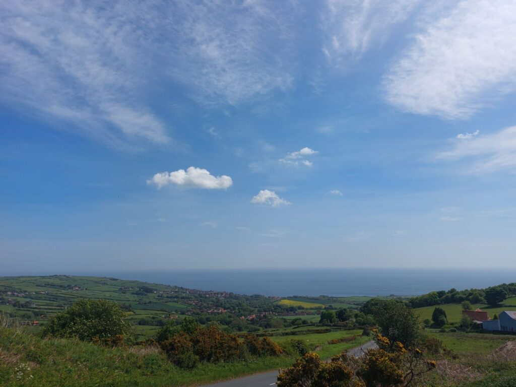 A view into the distance of a bright blue cloudless sky over roling lush green fields and hills