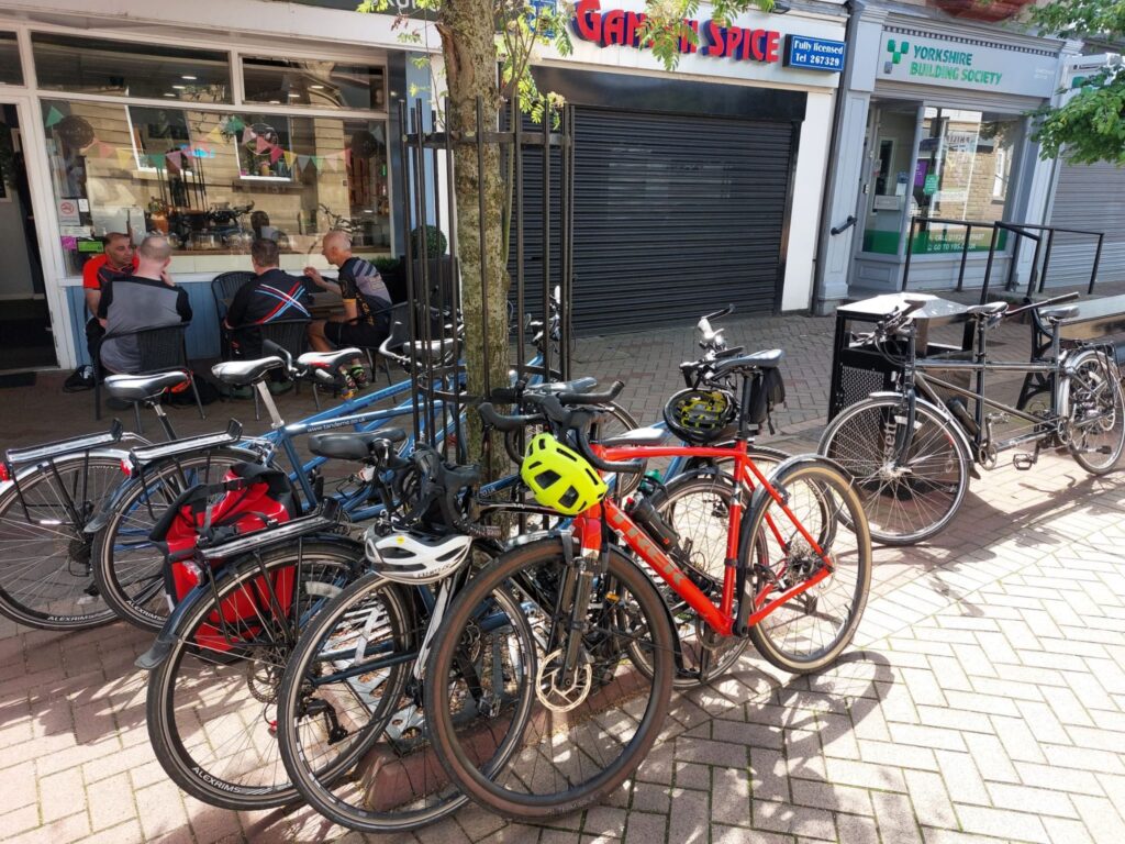 Several tandems bikes and a red solo bike propped up against street furniture including against a bin and against a railing around a tree